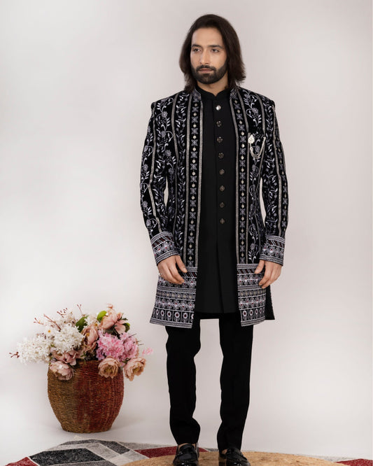 Man wearing a black and white patterned sherwani with a plain background