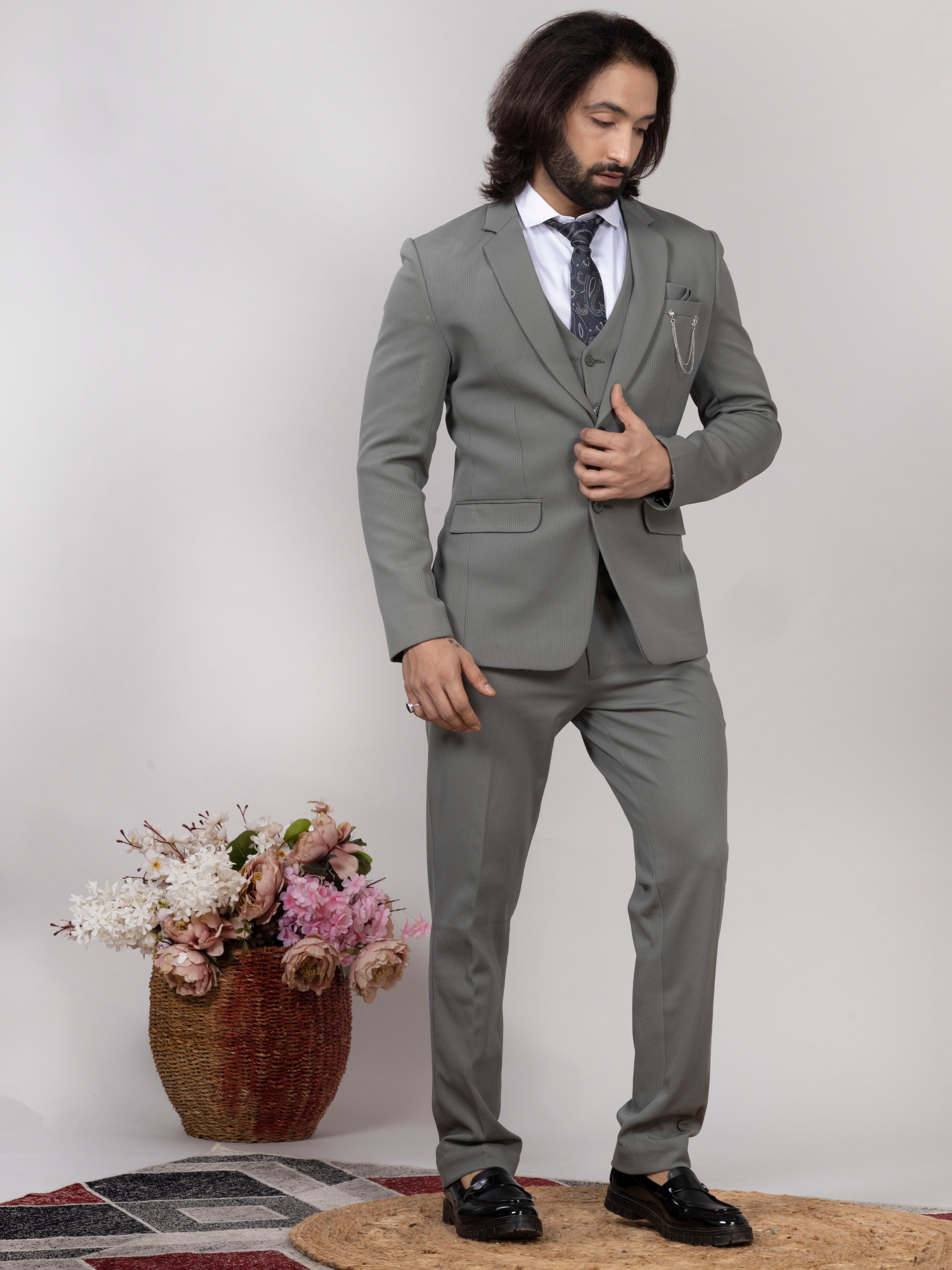 Man in a gray suit standing next to a decorative plant against a plain background