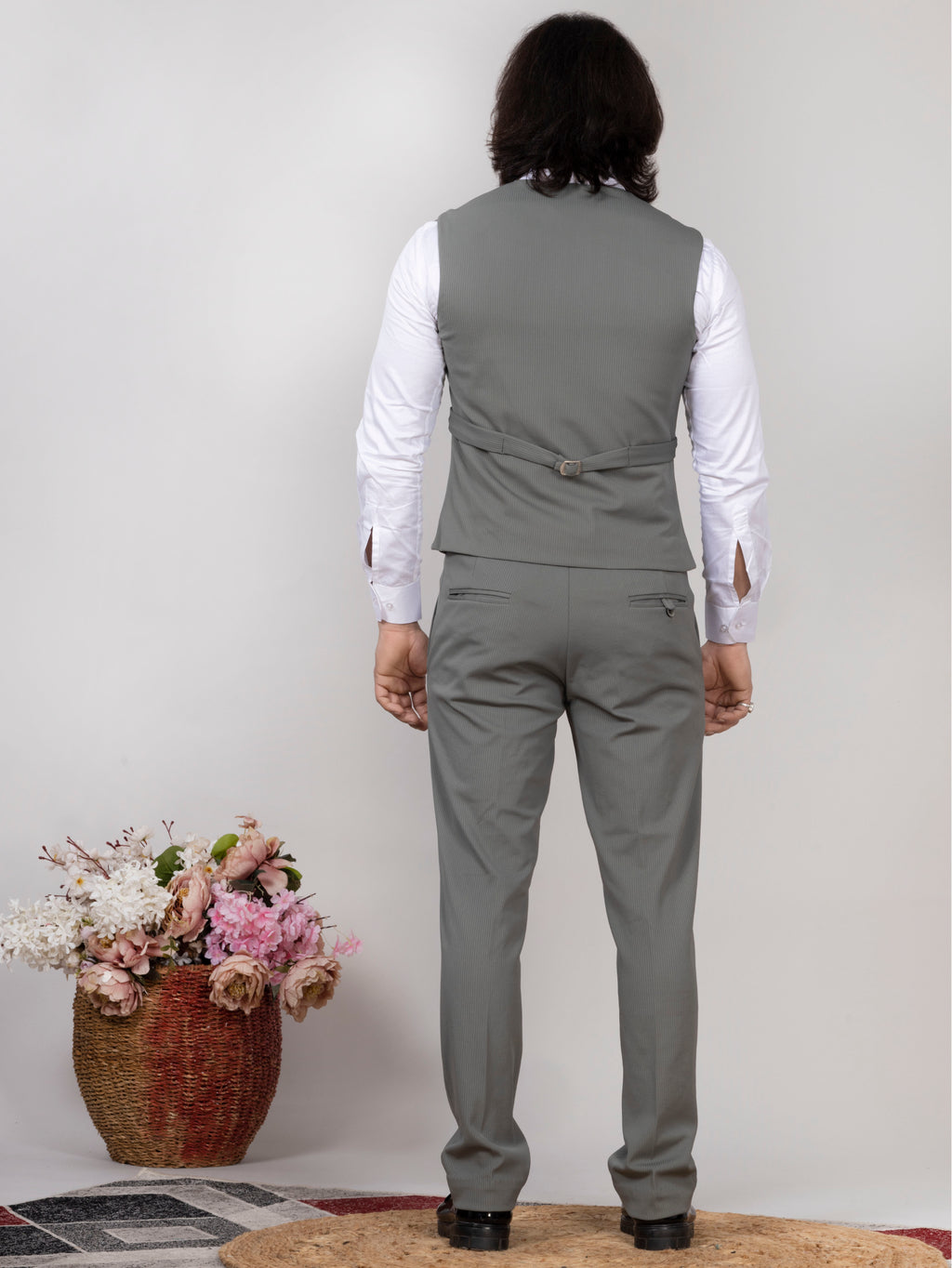 Person wearing a gray suit with a white shirt, standing against a plain background with flowers in the foreground.