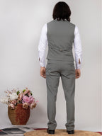 Person wearing a gray suit with a white shirt, standing against a plain background with flowers in the foreground.