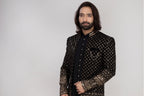 Man wearing a traditional embroidered sherwani with a vase of flowers in the background
