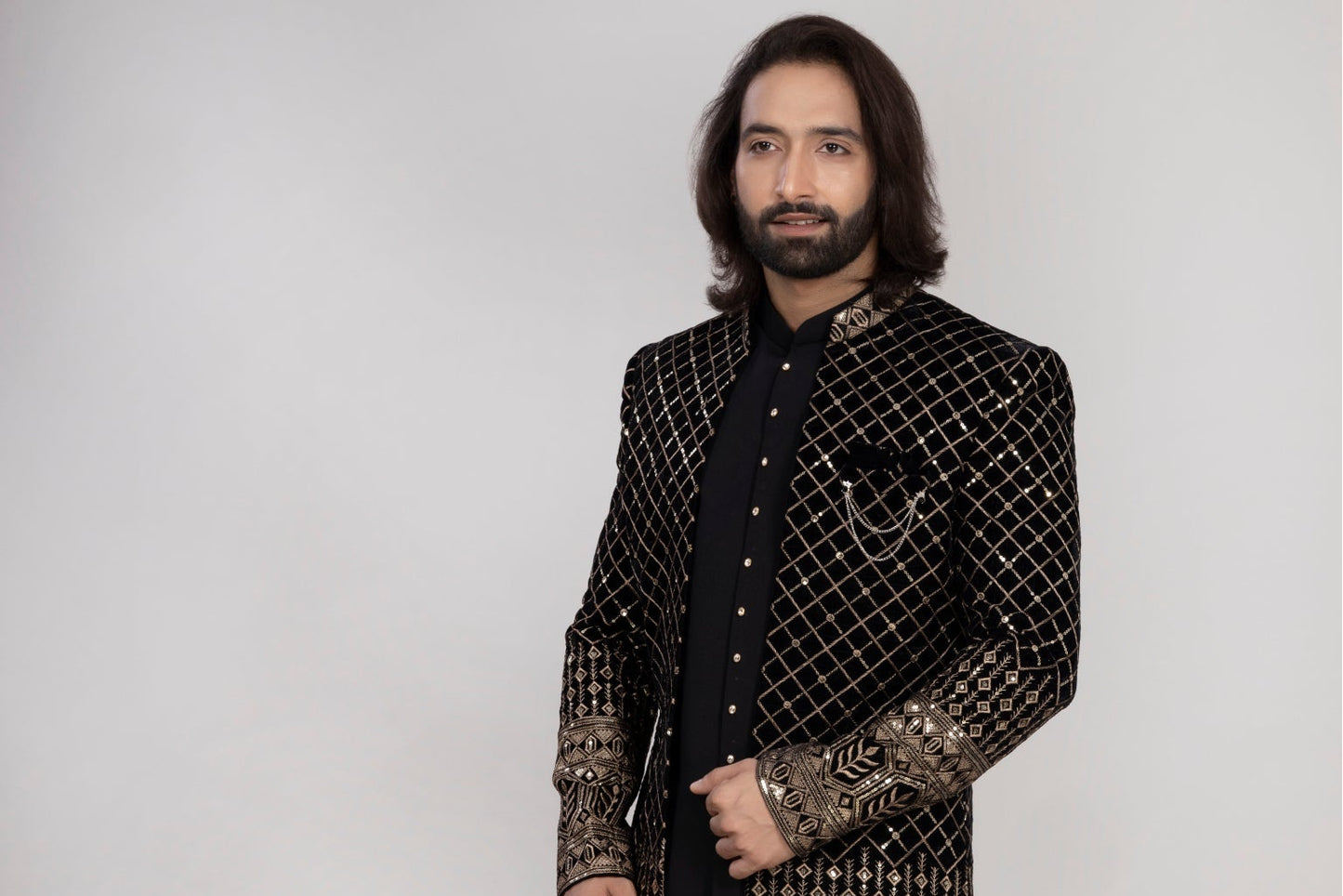 Man wearing a traditional embroidered sherwani with a vase of flowers in the background