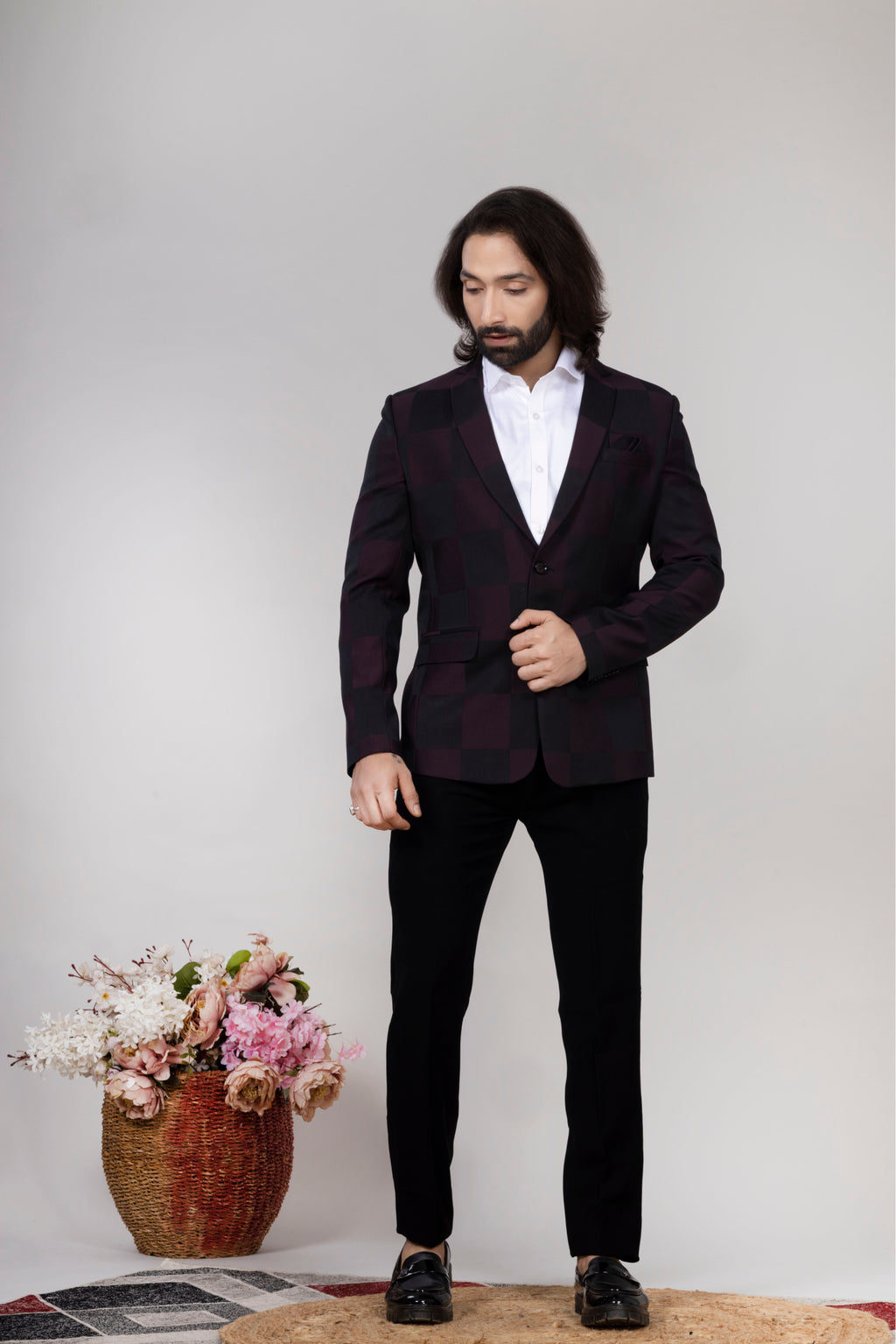 Man in a black suit standing next to a vase of flowers on a light gray background