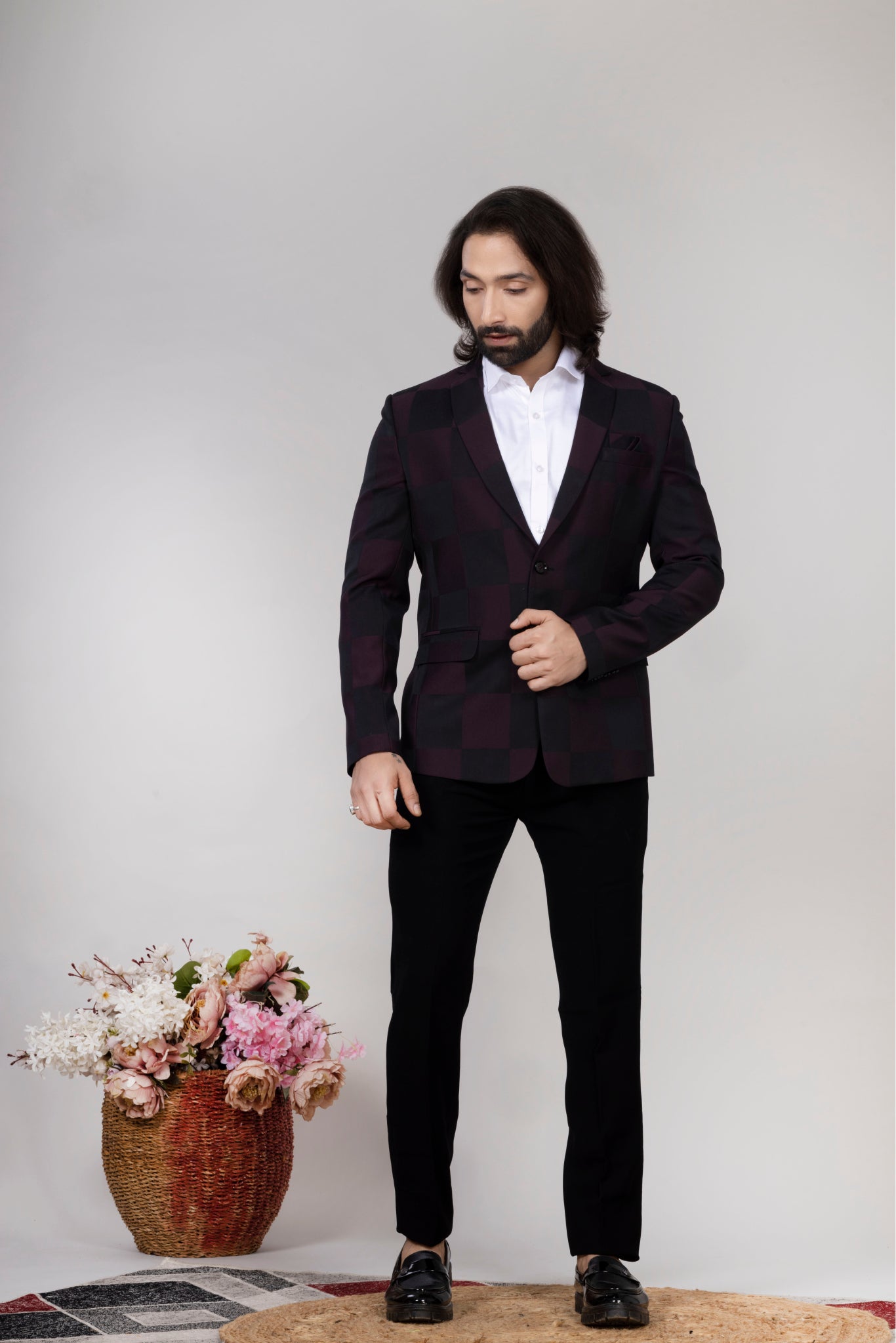 Man in a black suit standing next to a vase of flowers on a light gray background