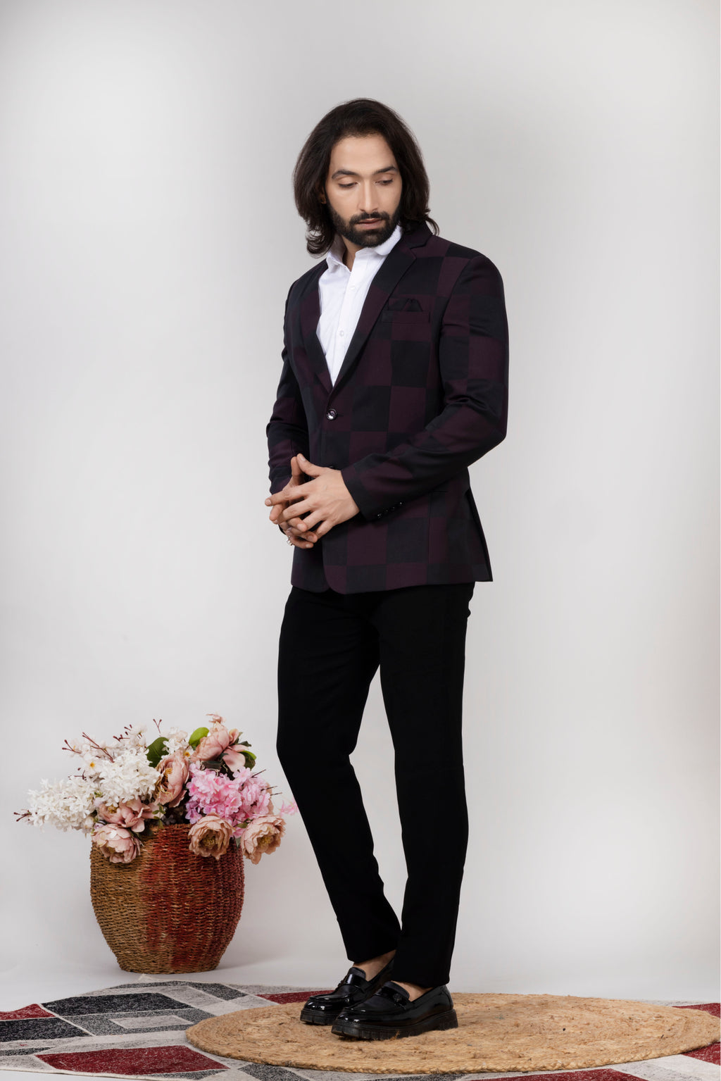 Man in a dark suit standing next to a vase of flowers on a patterned rug.