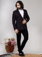 Man wearing a dark suit with a white shirt, standing against a plain background with a vase of flowers.