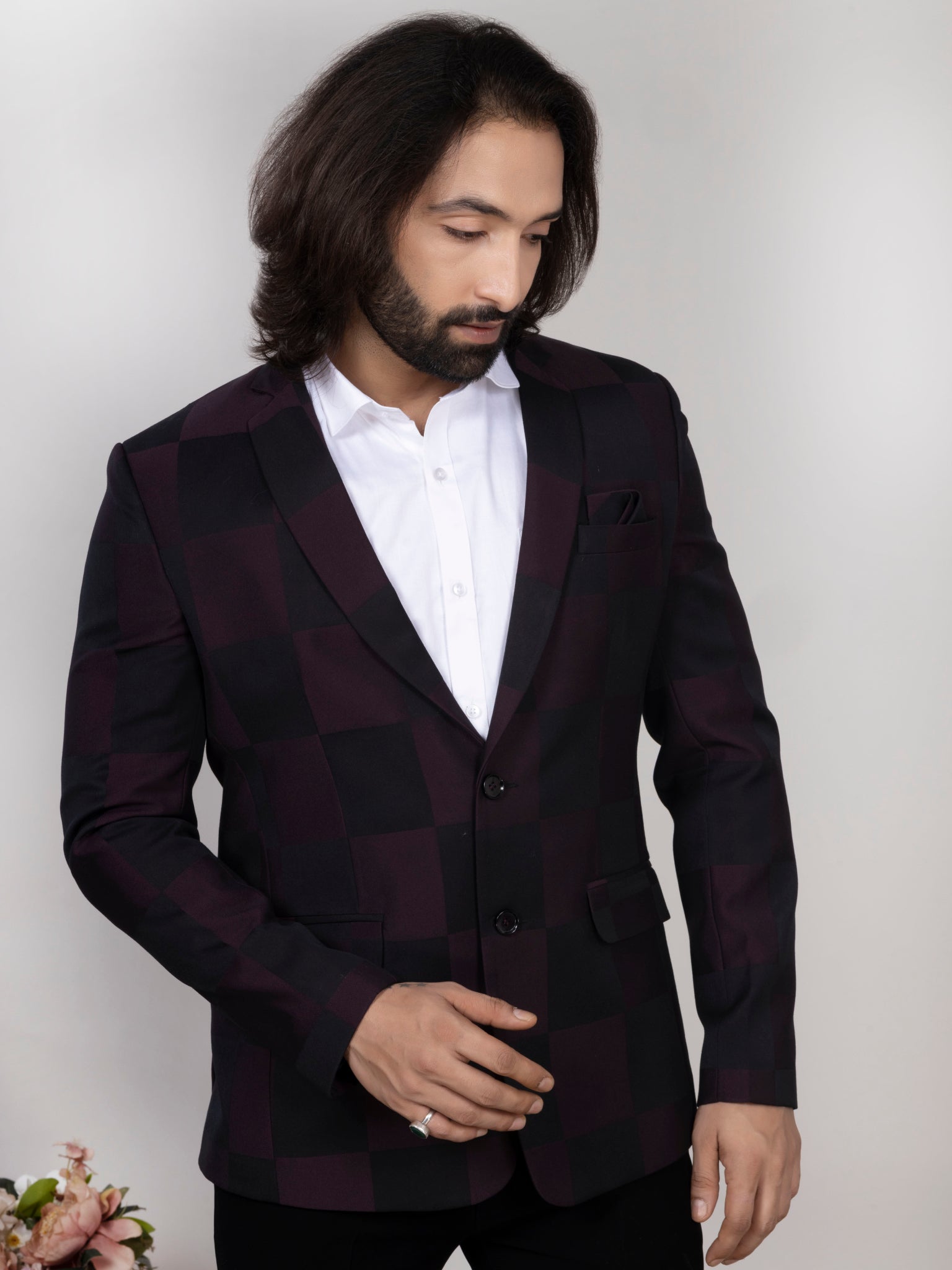 Man wearing a dark suit jacket over a white shirt against a plain background