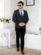 Man in a dark suit with a white shirt and brown shoes standing in a room with decorative elements.