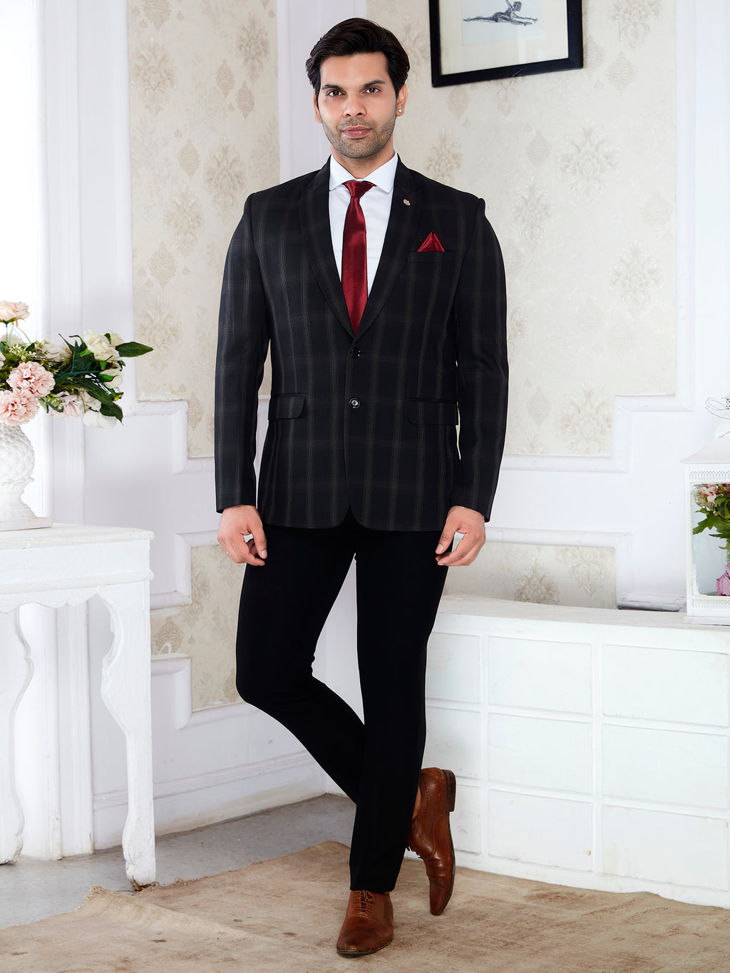 Man in a black pinstripe suit with a red tie standing in a decorated room.