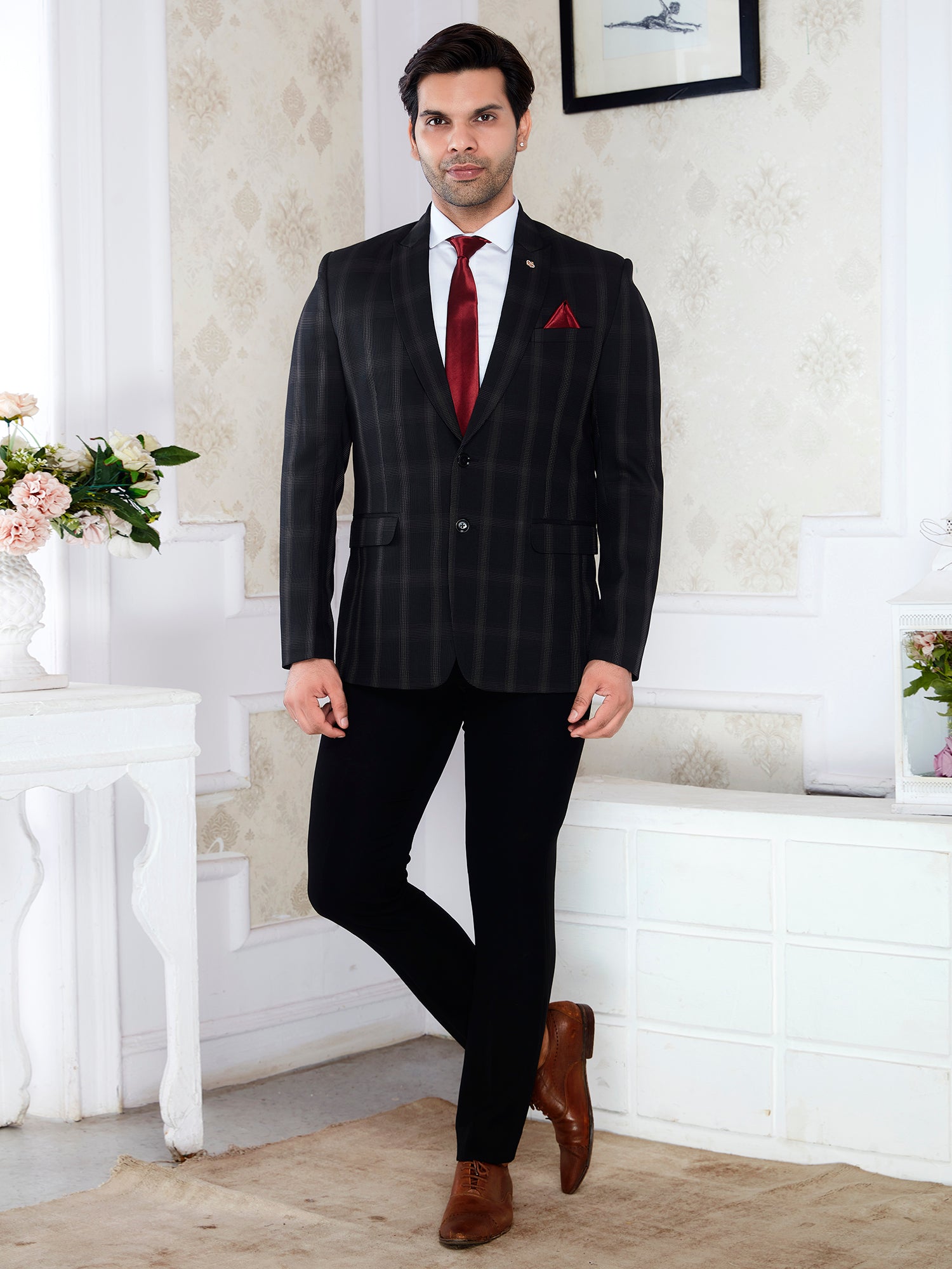 Man in a black pinstripe suit with a red tie standing in a decorated room.