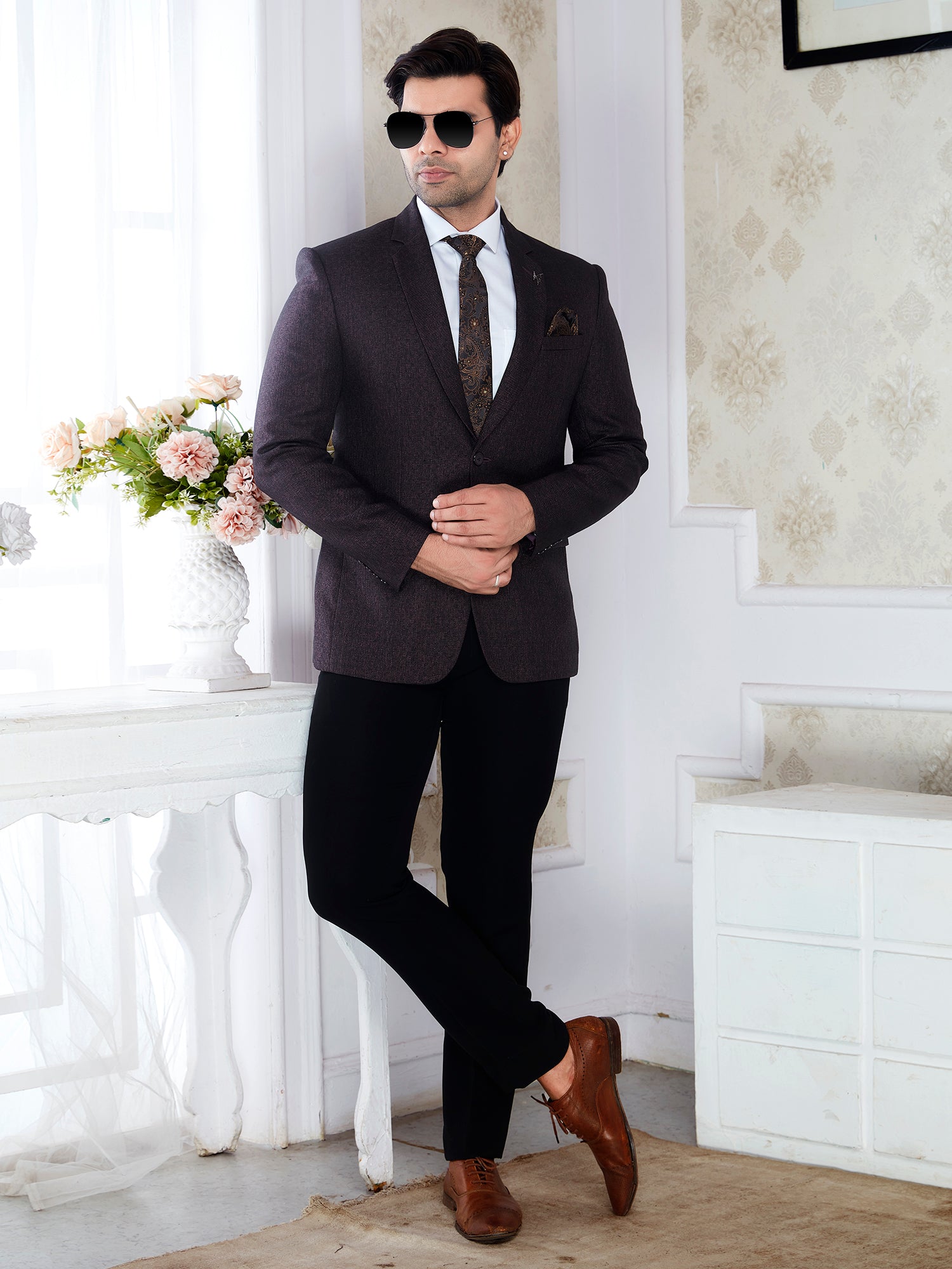 Man in a dark suit with sunglasses standing in a room with floral decor.