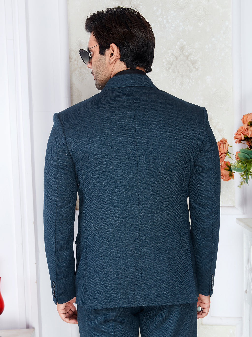 Man wearing a navy blue suit in an indoor setting with decorative elements.
