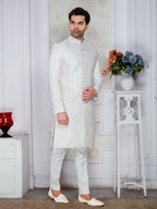 Man wearing a white sherwani in a decorated room with flowers and decor items.