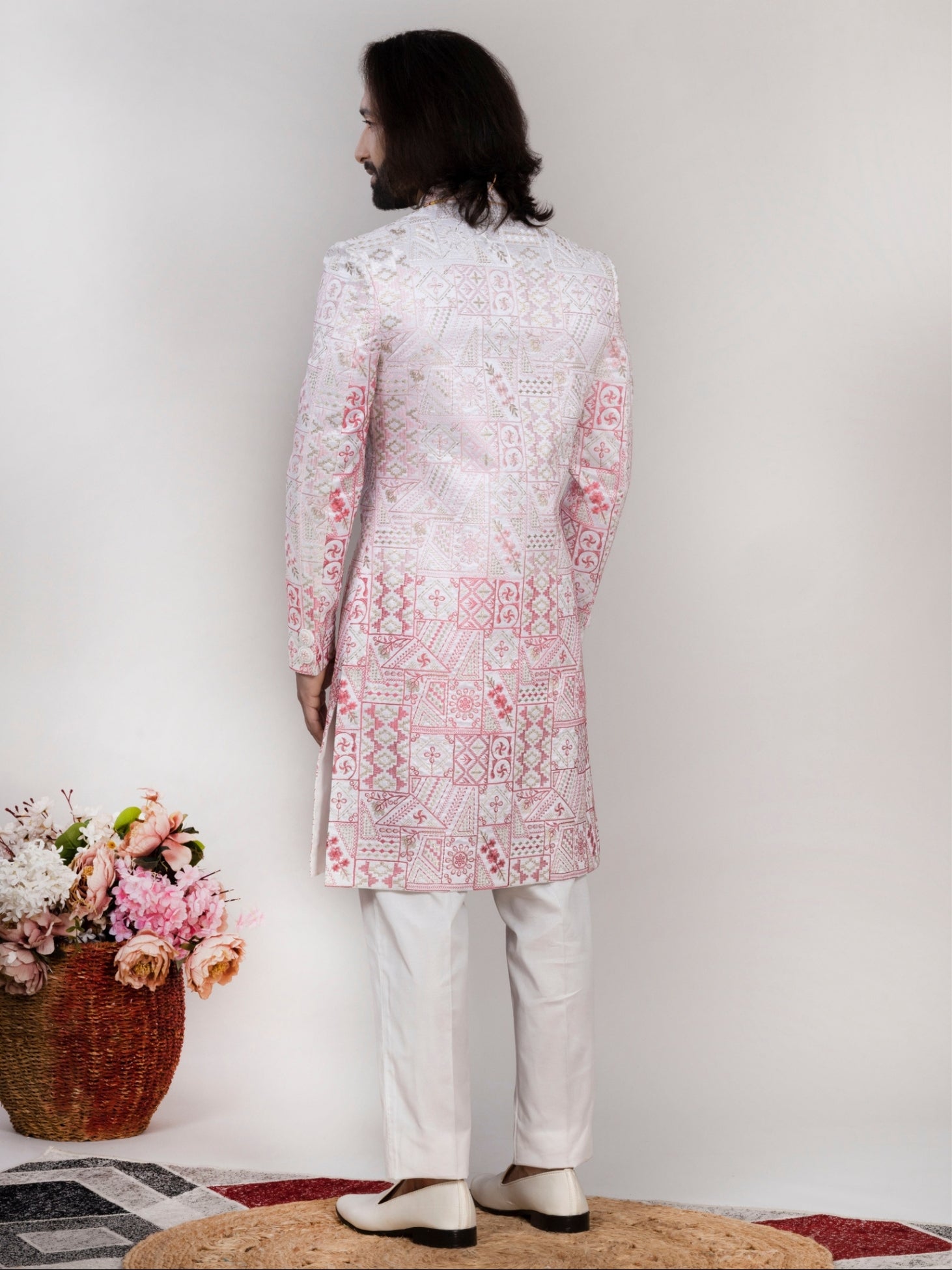 Man wearing a white and pink embroidered sherwani with a floral arrangement on a checkered floor.